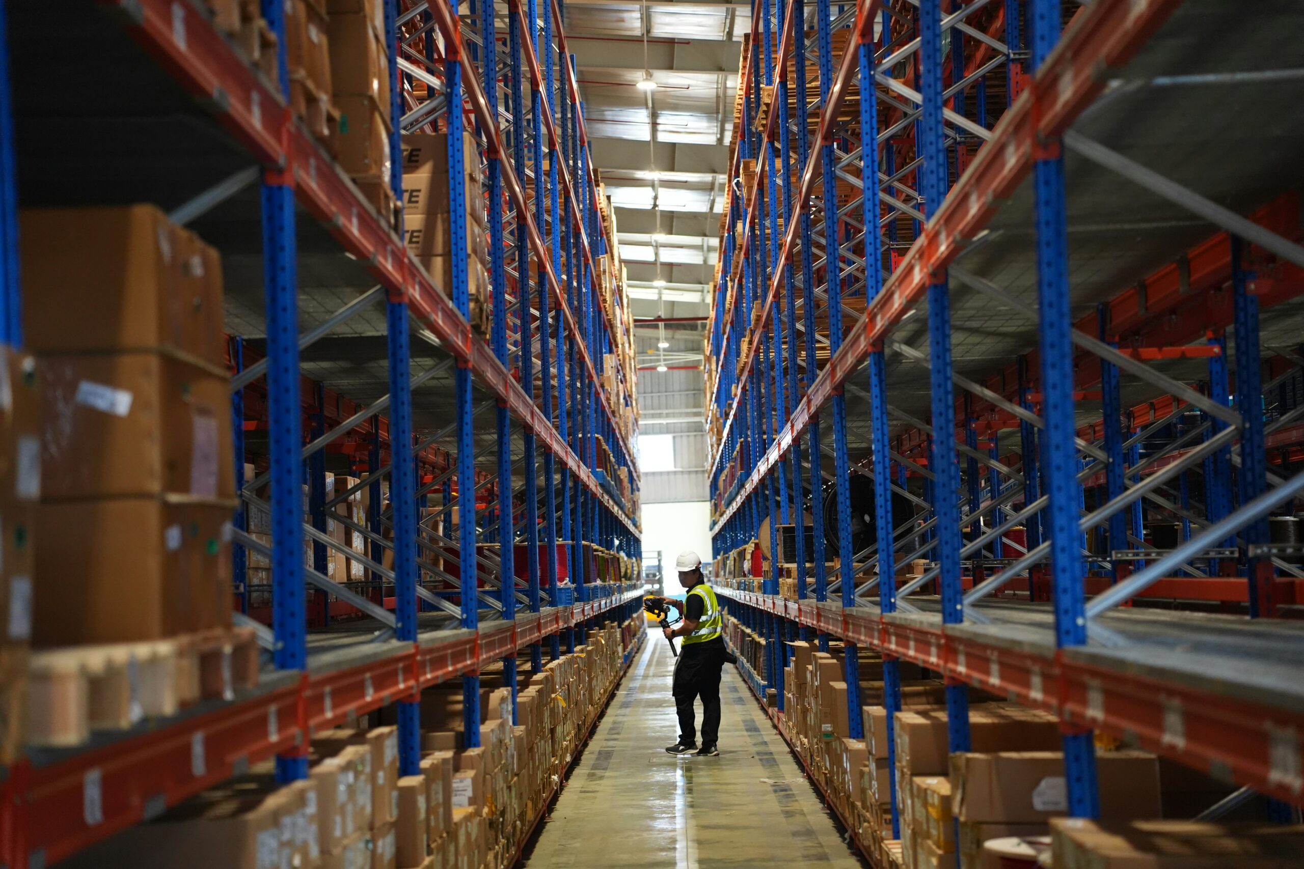 Warehouse worker walking through tall storage racks filled with boxes in a large distribution center
