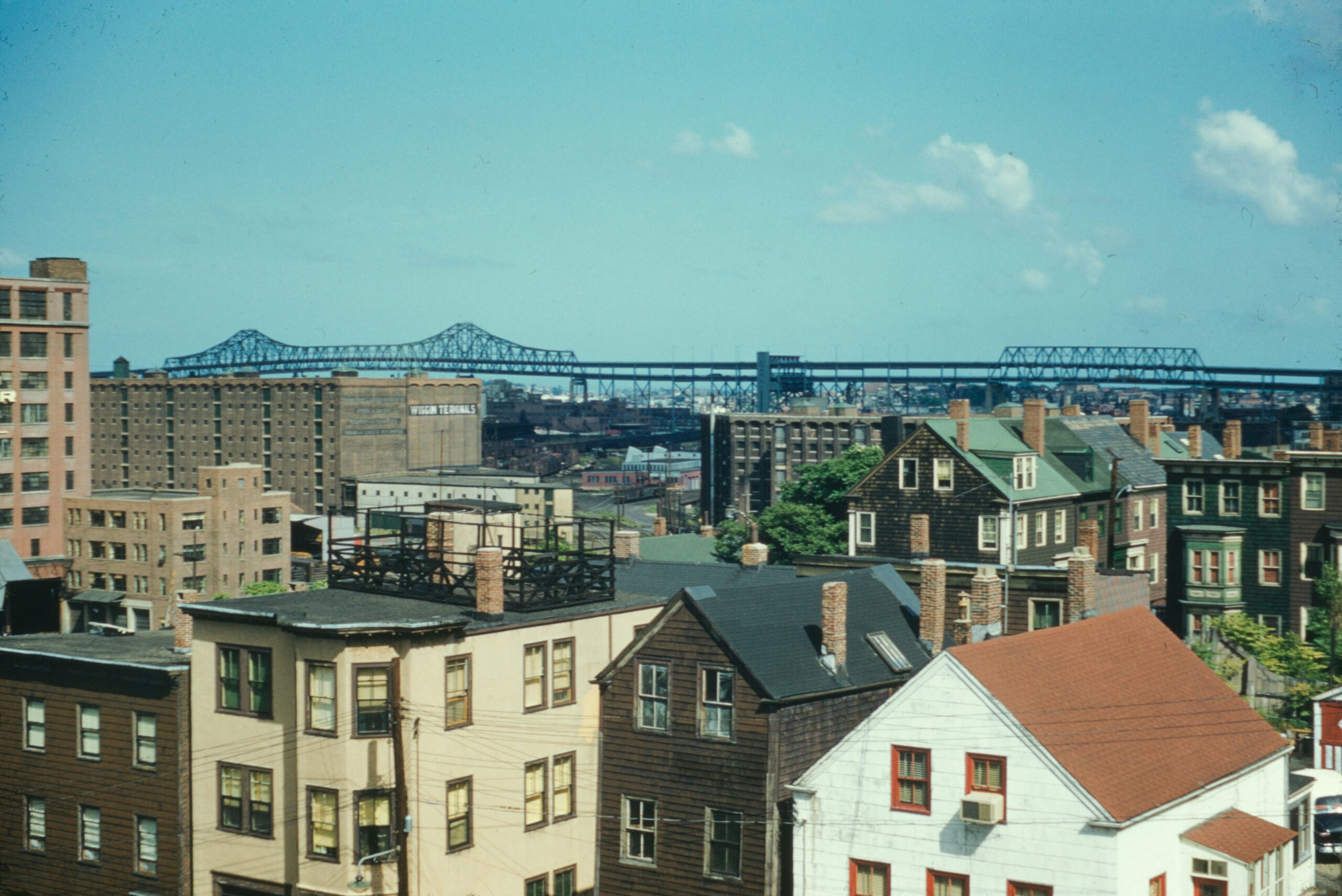 Aerial view of an urban neighborhood with multifamily housing, older residential buildings, and a large bridge in the background.